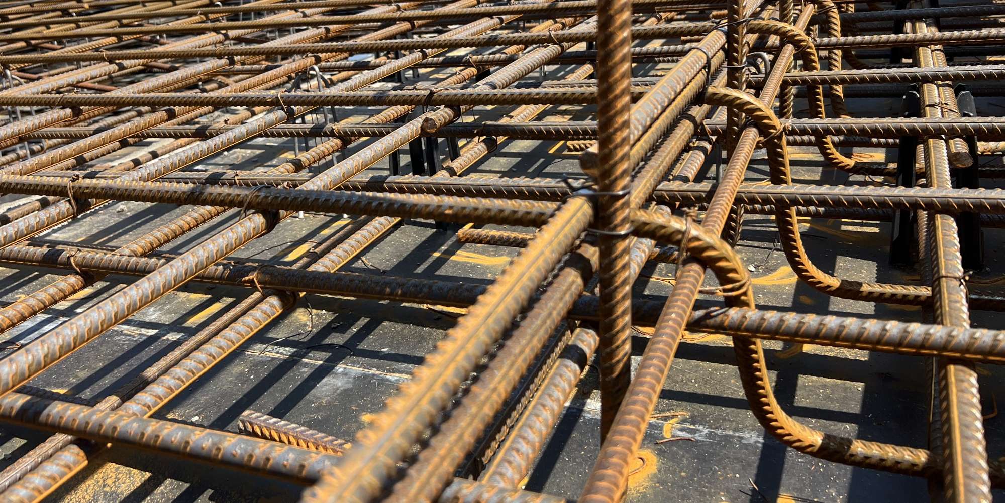 Close-up of intersecting steel rebar arranged in a grid pattern on a concrete base, commonly used for reinforcing concrete structures. The rusty rebar highlights the durability demands managed through expert labour hire services, ensuring robust construction even under harsh conditions.