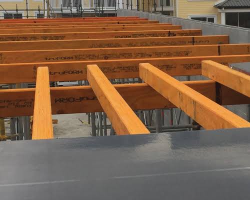 A partially constructed building showcases wooden beams supported by metal scaffolding, highlighting the precision and expertise provided by labour hire services. The beams are evenly spaced across a section, with some buildings visible in the background.